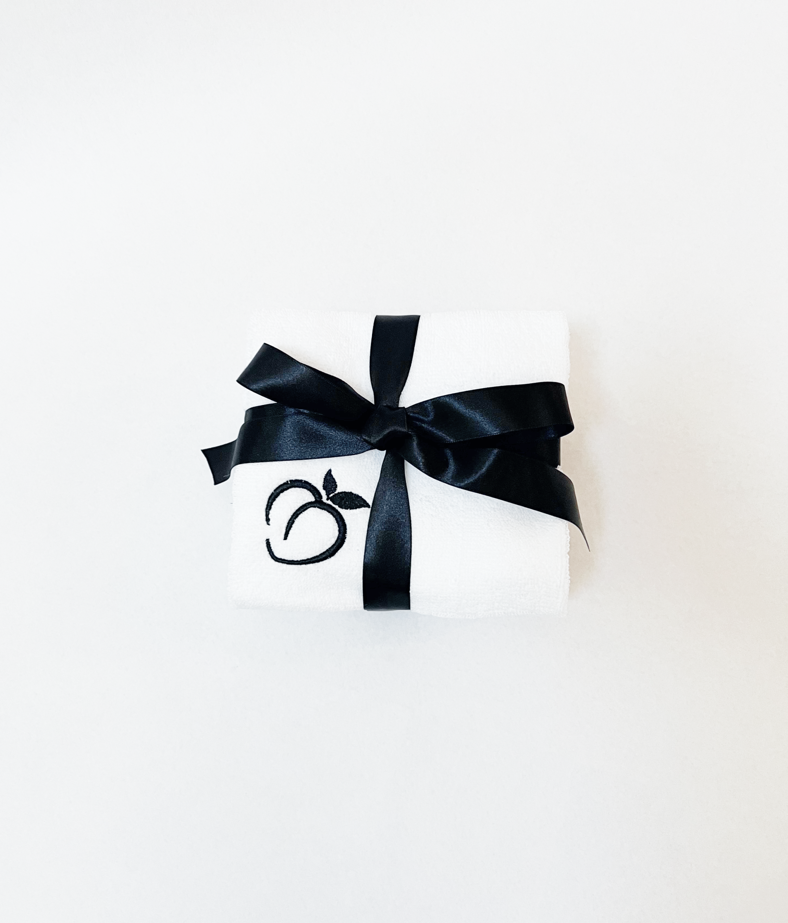 White Bumlicious 'Bum Rag' set embroidered with a peach logo and tied with a black satin ribbon, displayed on a clean white background.