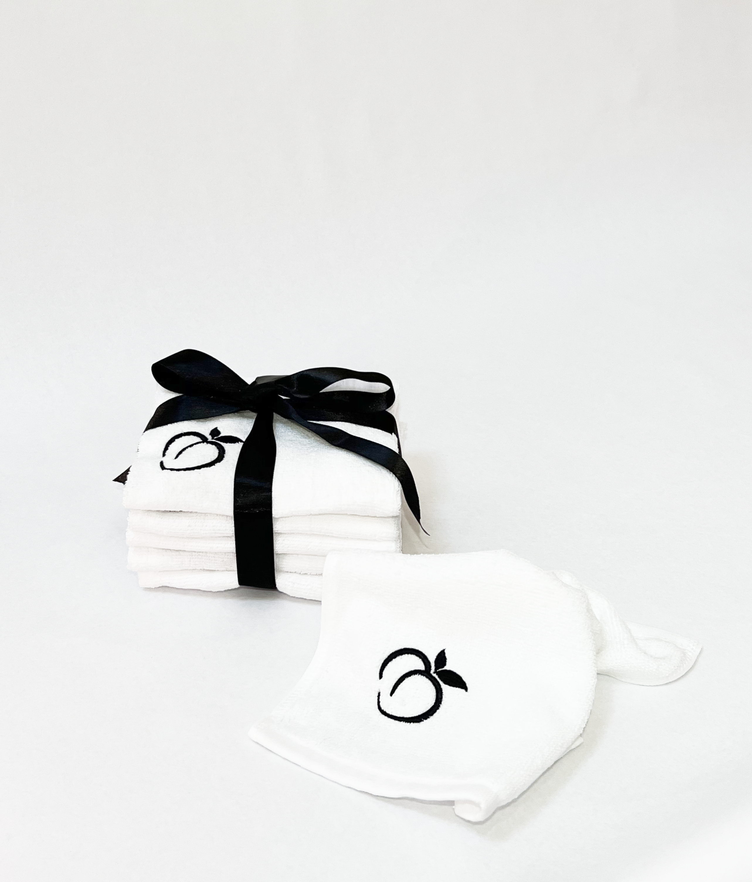 Stack of white Bumlicious Bum Rags embroidered with a Bumlicious peach logo and tied with a black satin ribbon, and a loose Bum Rag in front of it,displayed on a clean white background.
