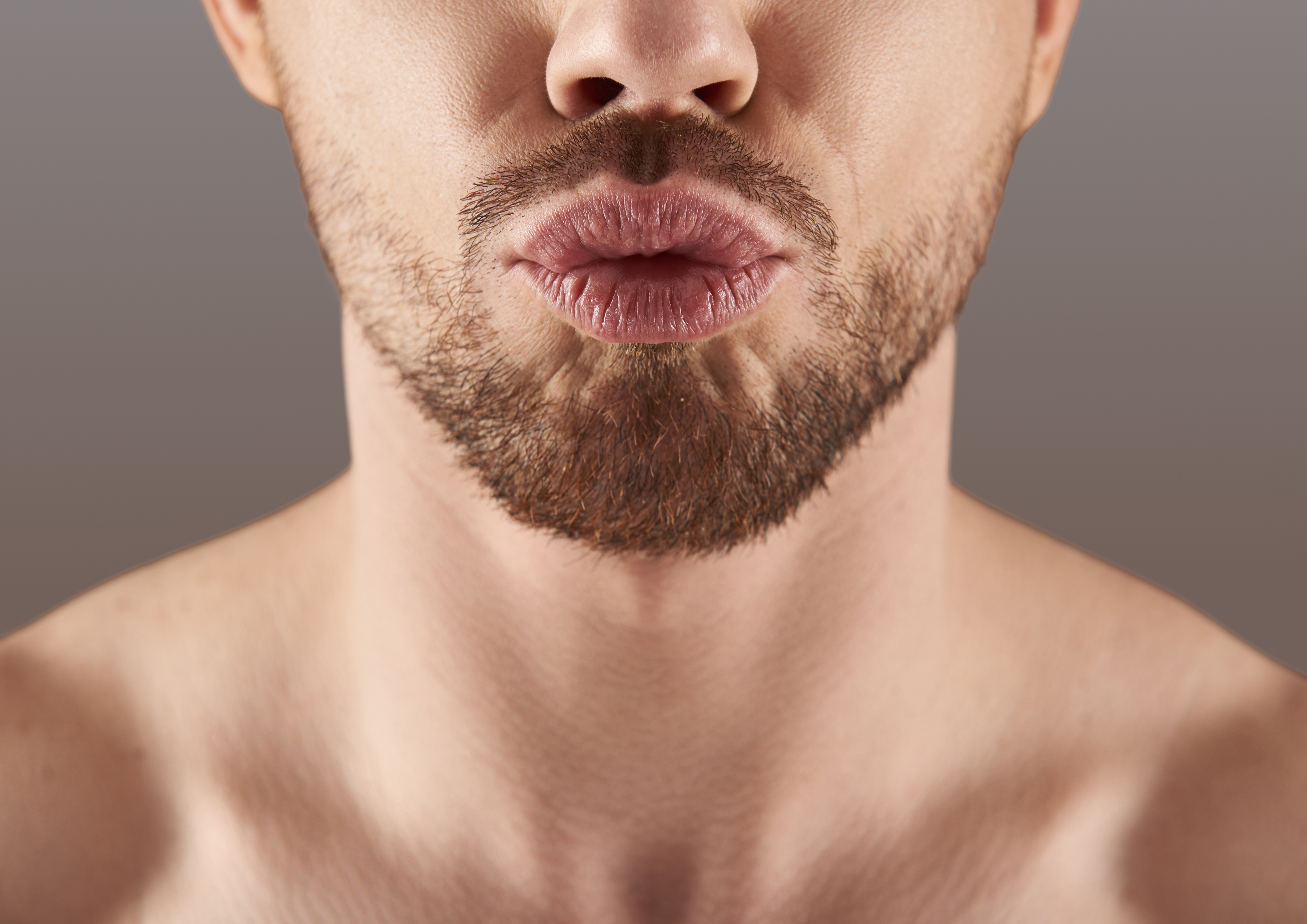 Close-up of a man's lips and beard against a neutral background