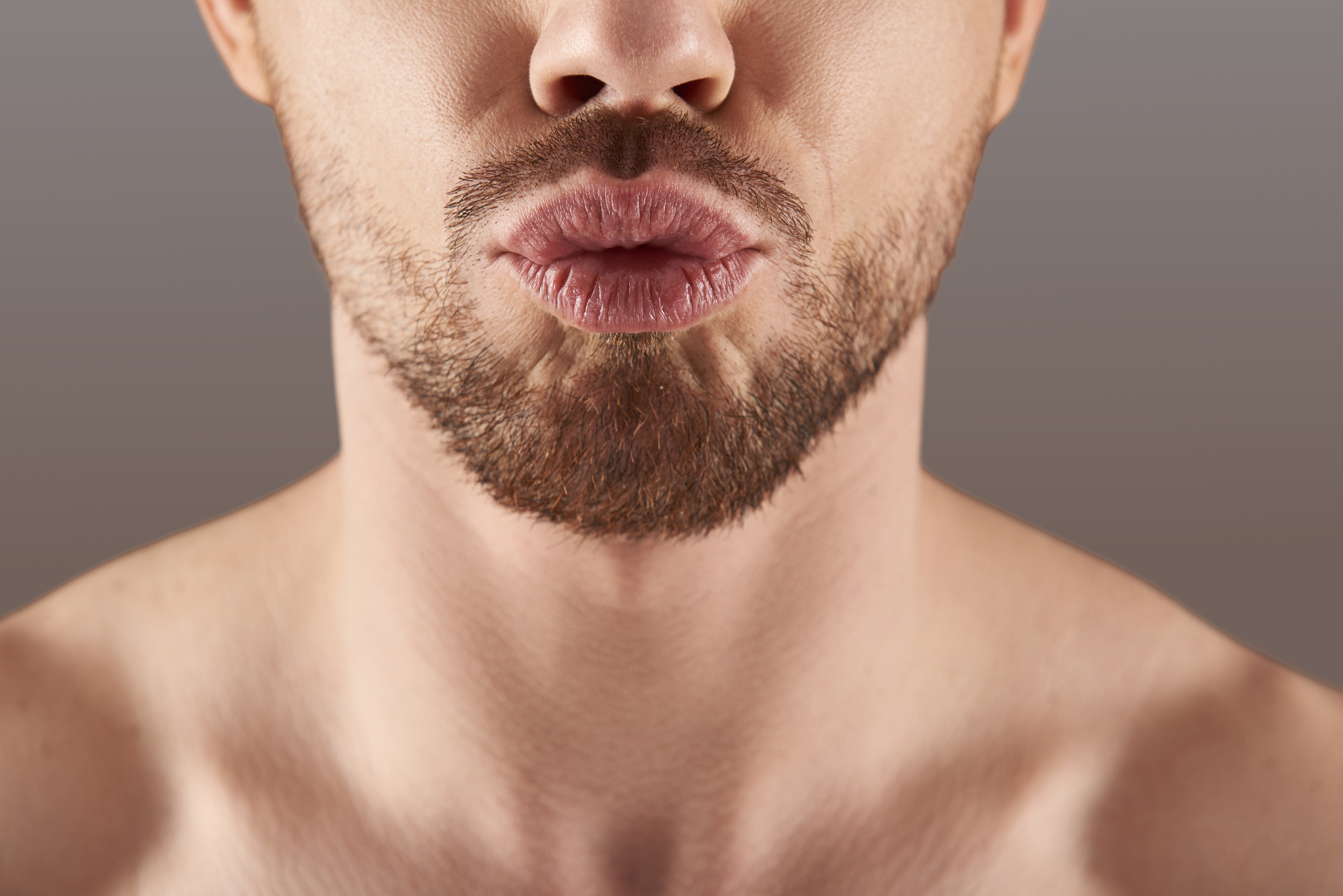 Close-up of a man's lips and beard against a neutral background