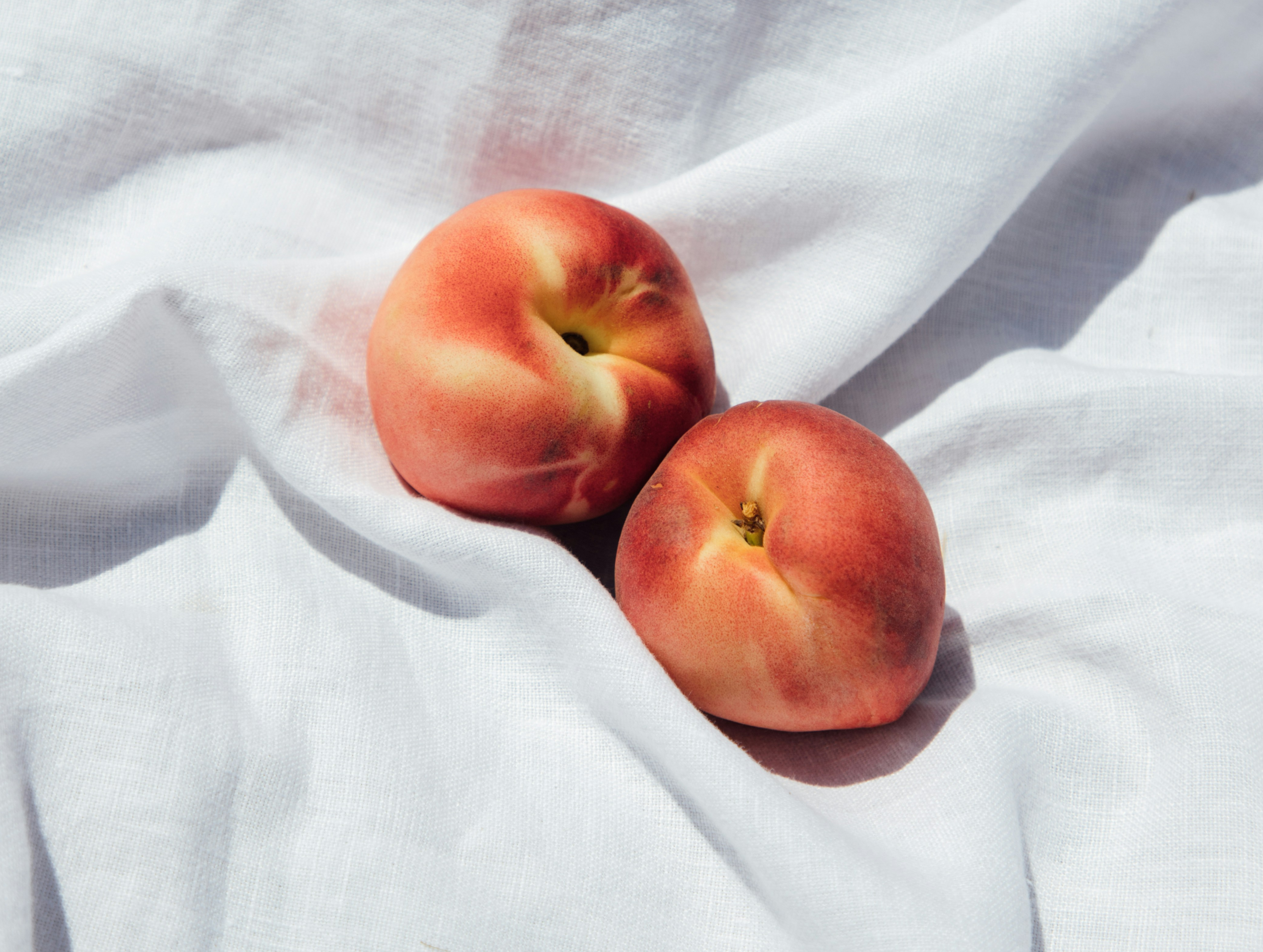 Two peaches on a white fabric background