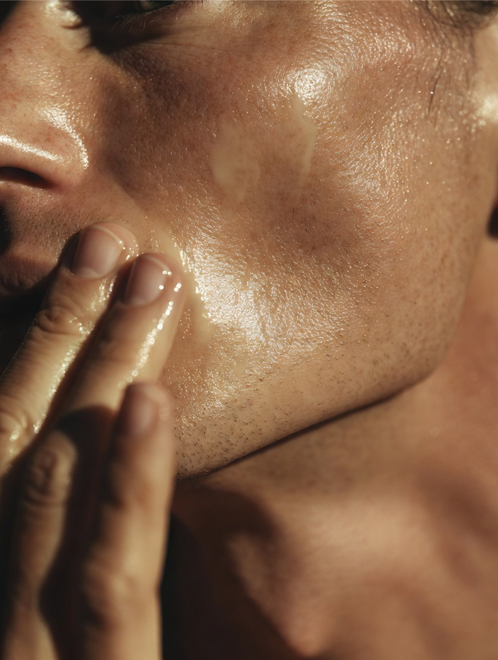 Close-up of a person's face with a hand touching the skin putting on the BUM OIL product, highlighting texture and lighting.